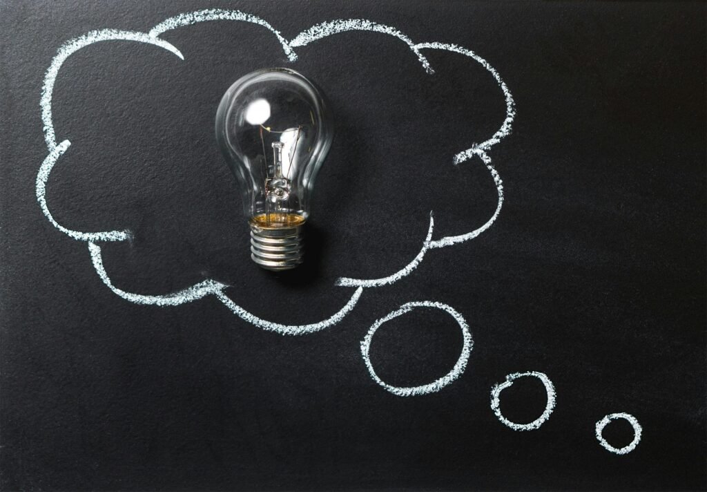 Light bulb laying on chalkboard with drawn thought bubble, symbolizing creative ideas.